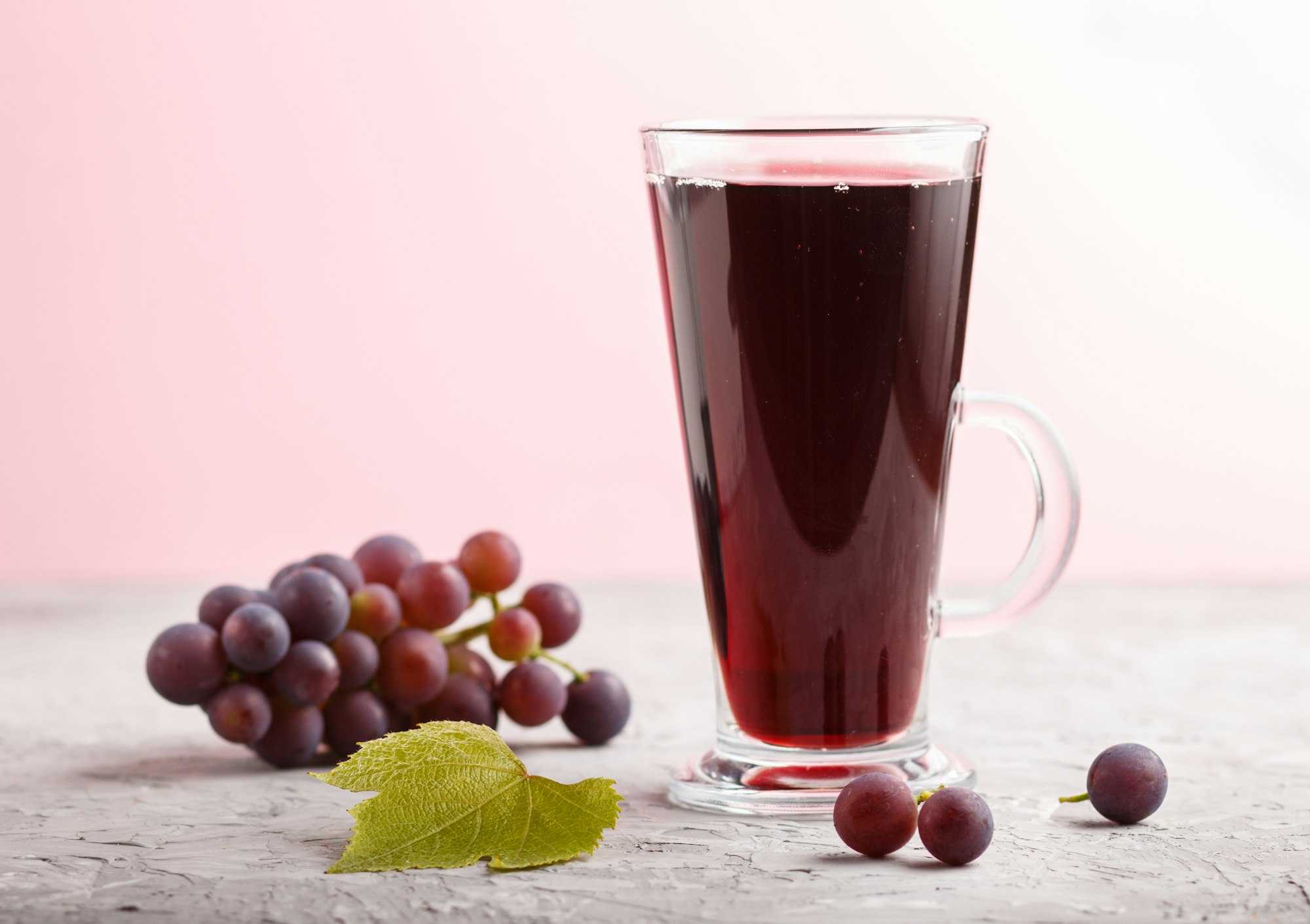 Glass of red grape juice on a gray and pink background. Side view